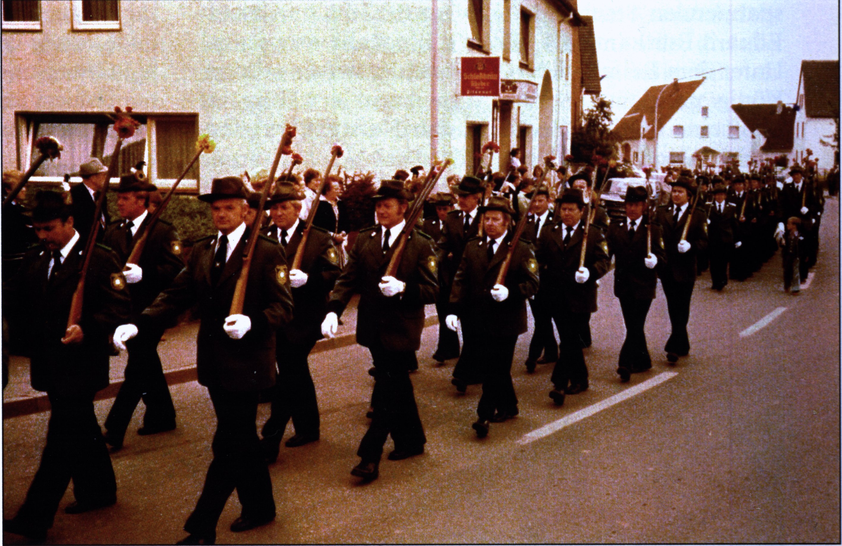 Schützen in grünen Uniformjacken marschieren mit geschulterten Holzgewehren im Gleichschritt durch den Ort Eissen.