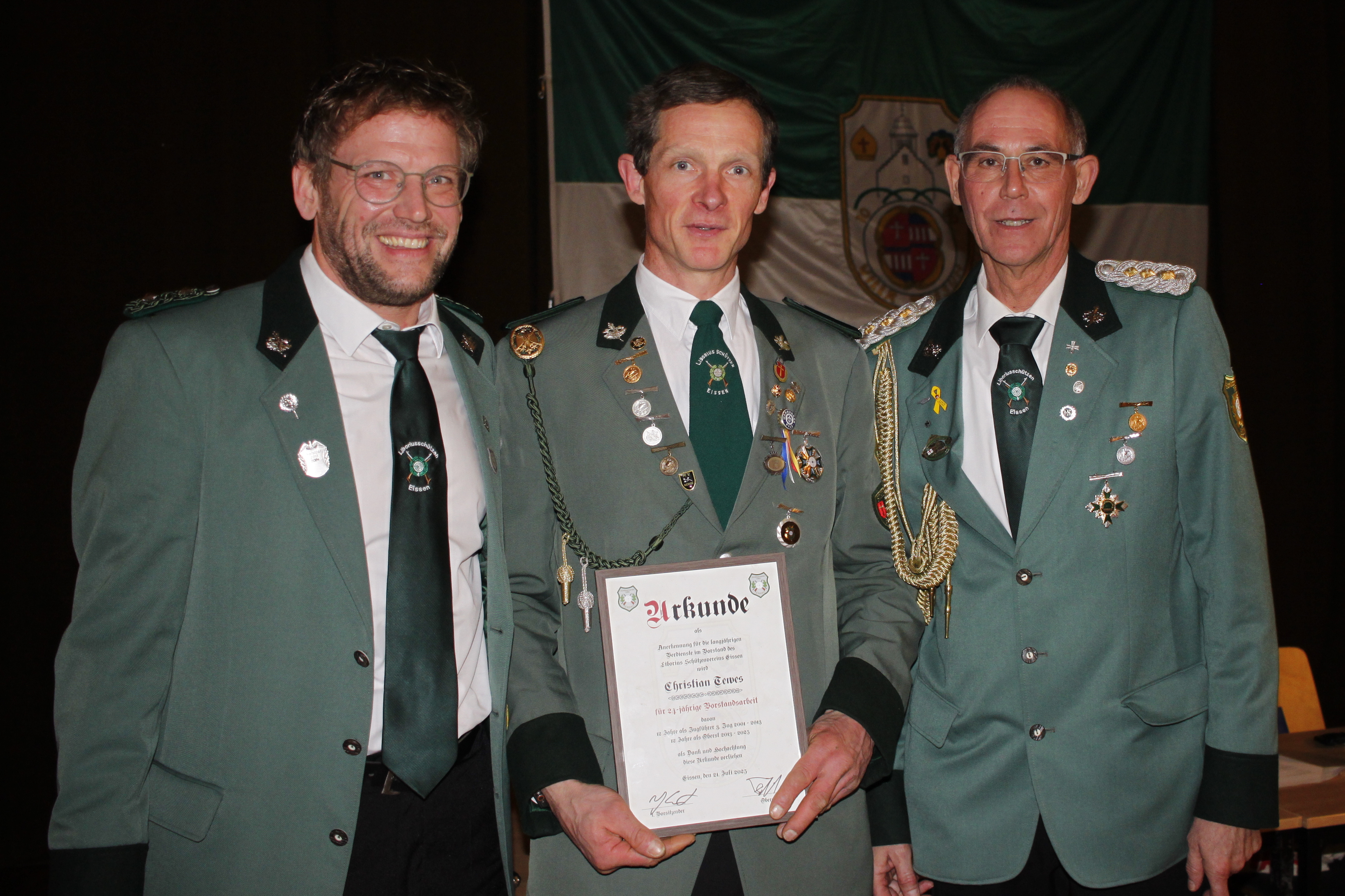 Drei Männer in grünen Schützenuniformen. Der Mann in der Mitte hält eine Urkunde.